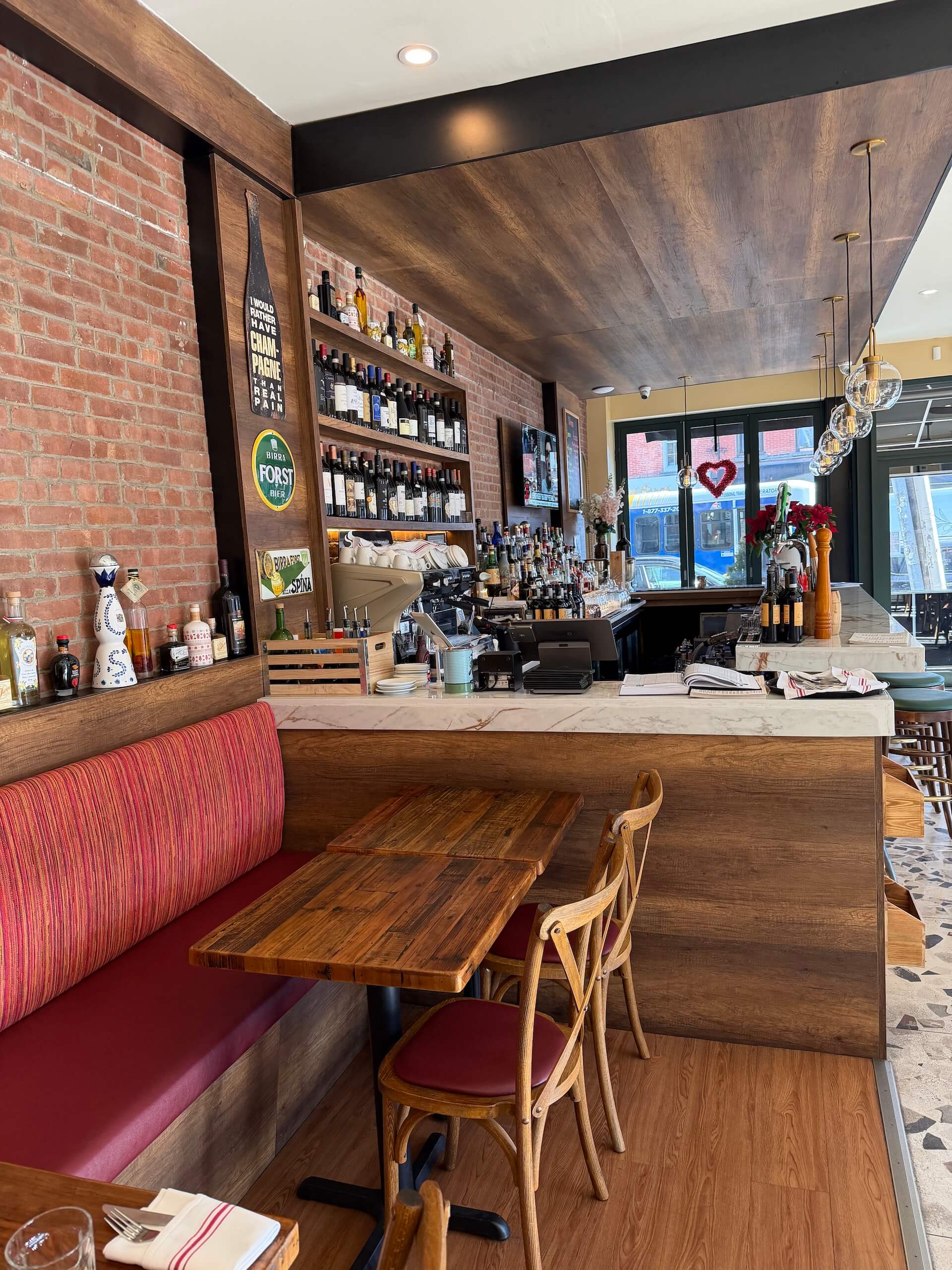 A red banquette and wooden tables in front of the brick wall and the bar